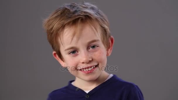 Beautiful little child smiling and giggling with a nervous body language for impatience and happiness, cuddling himself, grey background — Stock Video