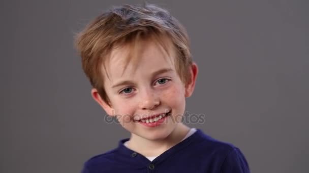 Hermoso niño pequeño sonriendo y riéndose con un lenguaje corporal nervioso para la impaciencia y la felicidad, abrazándose, fondo gris — Vídeos de Stock