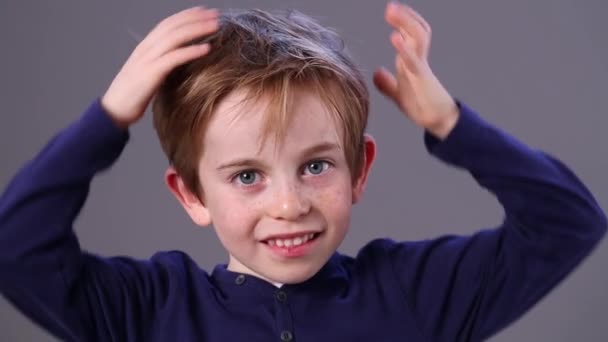 Sonriente adorable niño pequeño con pecas rascarse el pelo rojo — Vídeo de stock