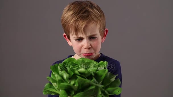 Unhappy beautiful child holding a green salad expressing aversion — Stock Video