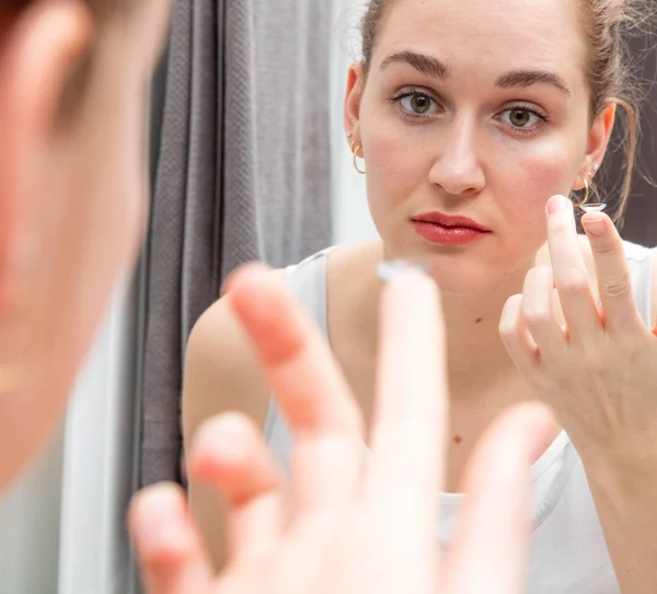 Joven hermosa mujer cambiando lentes de contacto delante del espejo — Foto de Stock