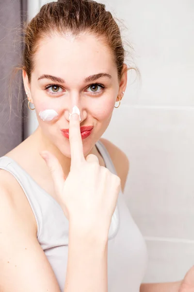 Hermosa mujer joven juguetona aplicando protector solar hidratante en su baño — Foto de Stock