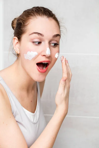 Alegre hermosa joven con el pelo atado aplicación de crema hidratante — Foto de Stock