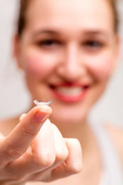 contact lens shown on the finger of blurred happy girl
