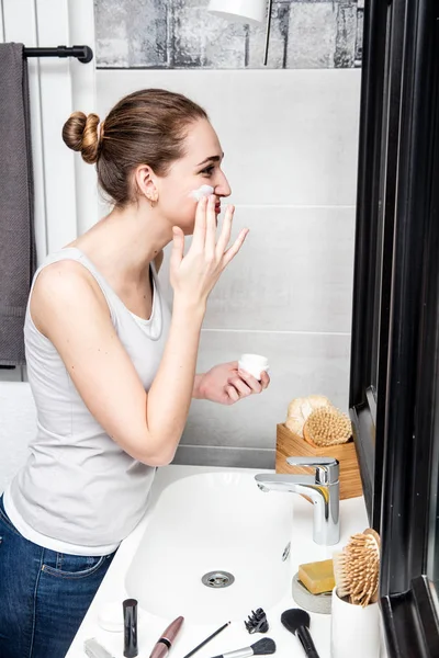 Hermosa mujer hidratando su cara en el baño con accesorios de maquillaje — Foto de Stock