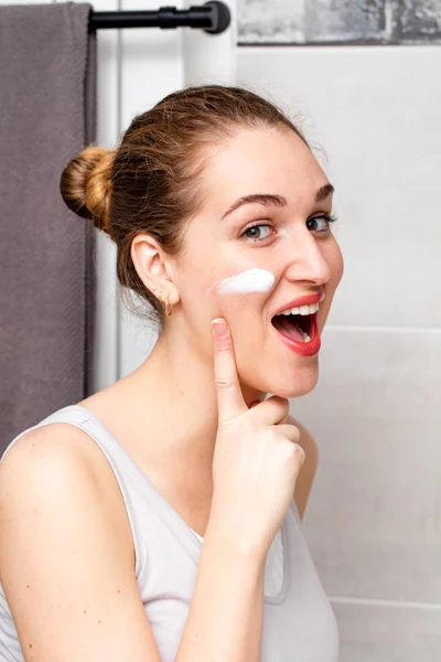 Laughing beautiful girl enjoying applying face cream on her cheek — Stock Photo, Image