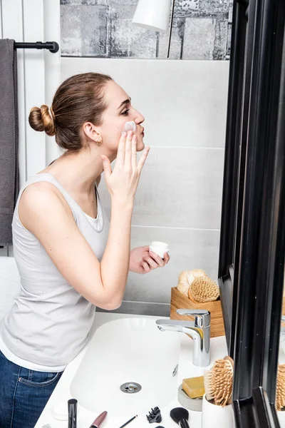 Hermosa chica aplicando crema en su cuarto de baño con accesorios de belleza — Foto de Stock