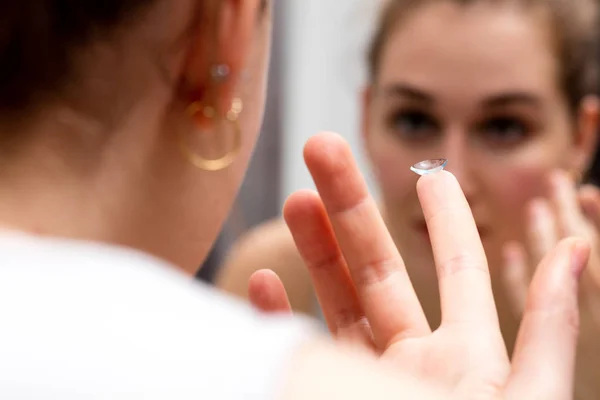 Молодая женщина смотрит в зеркало, чтобы сменить контактные линзы — стоковое фото