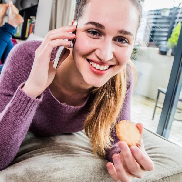 Cheerful gorgeous girl with a cookie talking on her phone — Stock Photo, Image