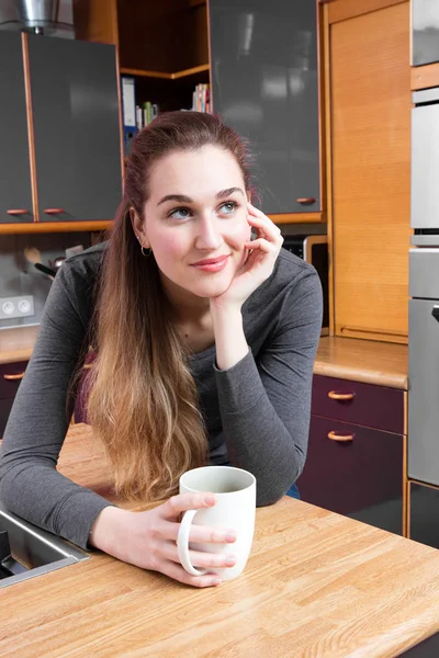 Dreaming beautiful girl relaxing with a coffee in kitchen, smiling — Stock Photo, Image