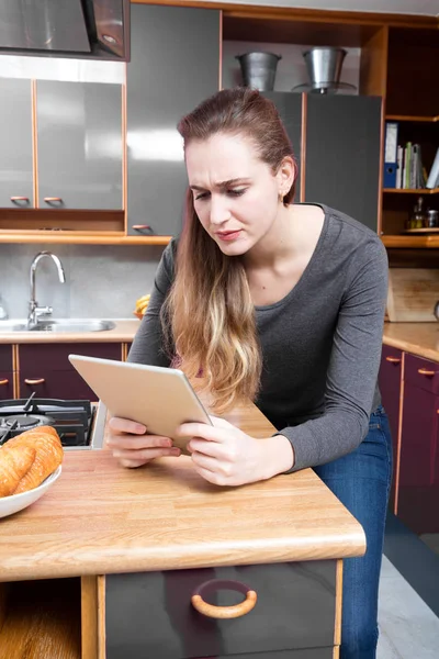 annoyed young woman frowning in reading on tablet in kitchen