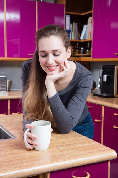 Hermosa joven sonriendo con su café sobre un fondo de cocina — Foto de Stock