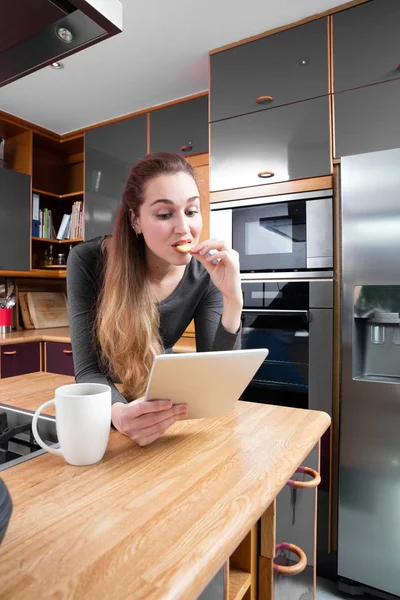 Chica sorprendida leyendo sus divertidos mensajes en la tableta, comer galletas — Foto de Stock