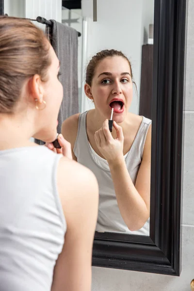 Sexy joven aplicación de su lápiz labial y brillo con espejo — Foto de Stock