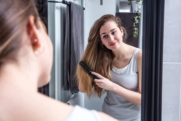 Atractiva joven mujer cepillando el pelo largo delante del espejo — Foto de Stock