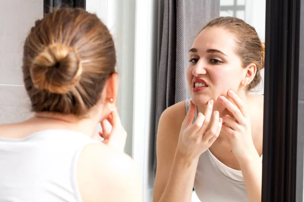 Mirror reflection of girl with acne squeezing her pimples — Stock Photo, Image