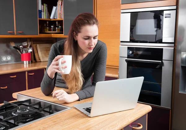 Concepto de casa de trabajo-dudosa hermosa mujer joven comprobar su ordenador portátil — Foto de Stock