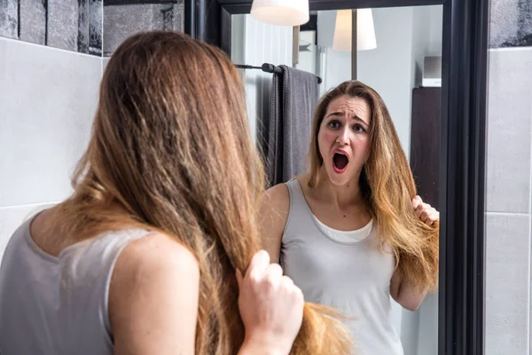 Sorprendida mujer joven infeliz revisando su cabello largo y seco — Foto de Stock