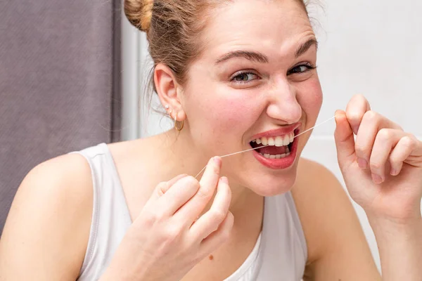 Dişleri temizlemek için diş ipi tutan güzel genç kadın çatık — Stok fotoğraf