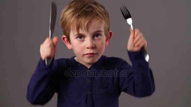 Голодный красивый маленький ребенок трясет вилкой и голодает ножом — стоковое видео