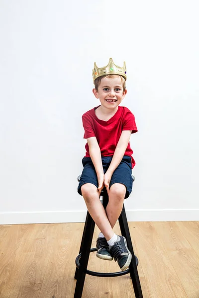 Ontspannen glimlachend jongetje met een kroon erboven zit op kruk — Stockfoto