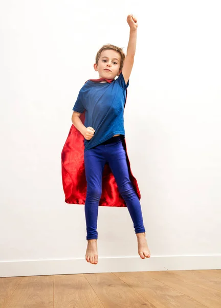 Poderoso menino super-herói com uma capa pulando alto, alcançando a liberdade — Fotografia de Stock