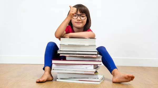 Niño sonriente sentado detrás de muchos libros con un pulgar hacia arriba —  Fotos de Stock