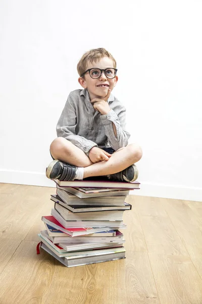 Happy smart child seated on top of books having idea — Stock Photo, Image