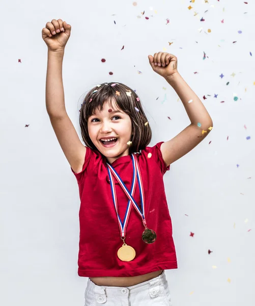 Éxito hermoso niño riendo con medallas de campeón, celebrando sobre confettis — Foto de Stock