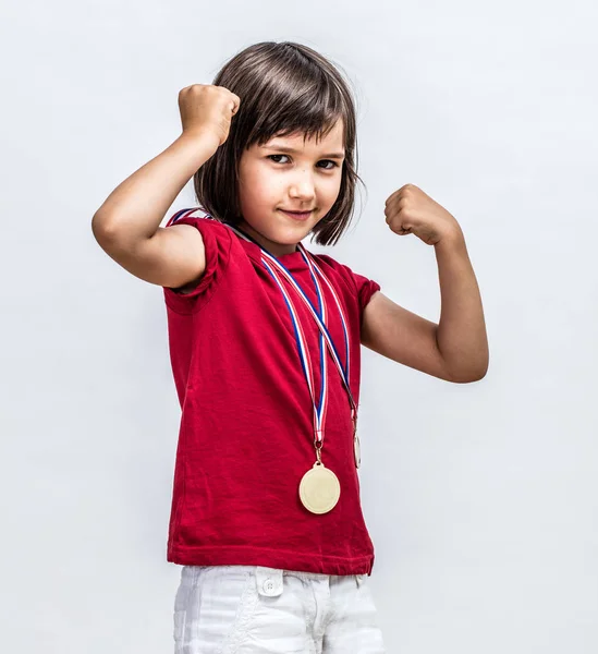 Маленька нахабна дівчинка з медалями посміхається, показуючи молоду жіночу силу — стокове фото