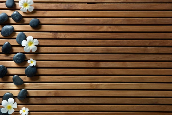 Cailloux de massage noirs et fleurs de spa fixés sur une planche en bois — Photo