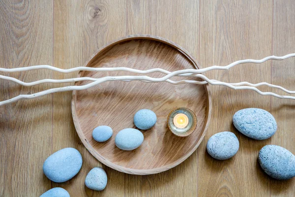 still-life of feng shui beauty, mindfulness, meditation and massage with a flow of zen pebbles, a candle and twigs over round wooden tray, top view
