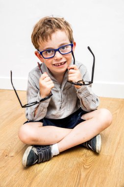 Gülümseyen çocuk yeni gözlük seçmekten zevk alıyor, göz bakımı için ikilem yaşıyor