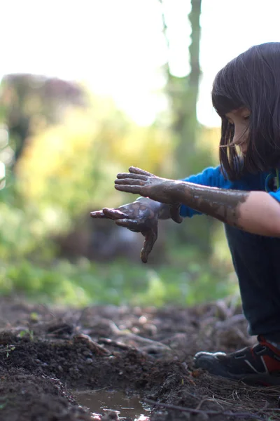 Bahçede oynayan, ellerindeki çamuru izleyen eğlenceli bir çocuk. — Stok fotoğraf