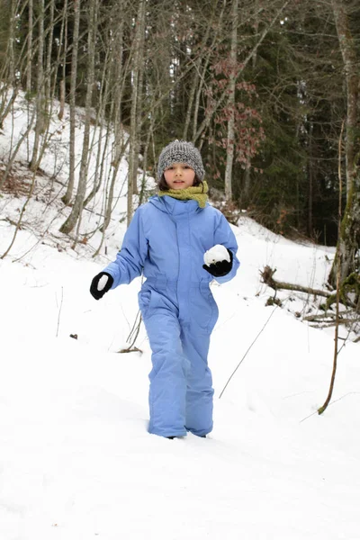 Smiling child with winter clothes hiking with snowballs, woods background — 스톡 사진
