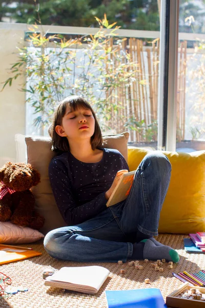 sad child leaning on cushions, bored of playing and studying for homeschooling in corona virus lockdown and school shutdown in sunny apartment