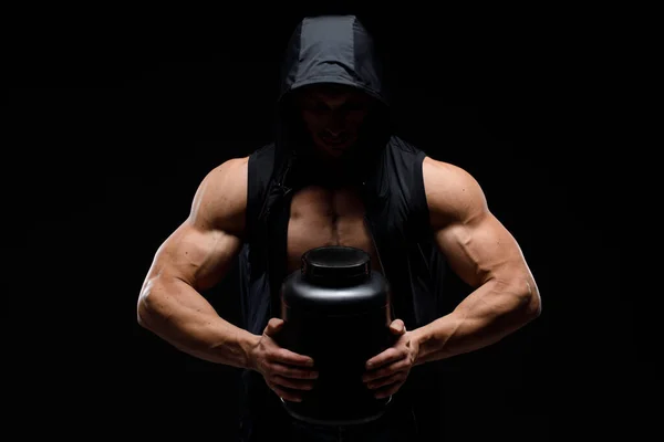Siyah arka planda protein kavanozu olan kaslı vücut geliştirici. Spor beslenmesi. Vücut geliştirme destek malzemeleri, spor, egzersiz, sağlıklı yaşam tarzı konsepti.