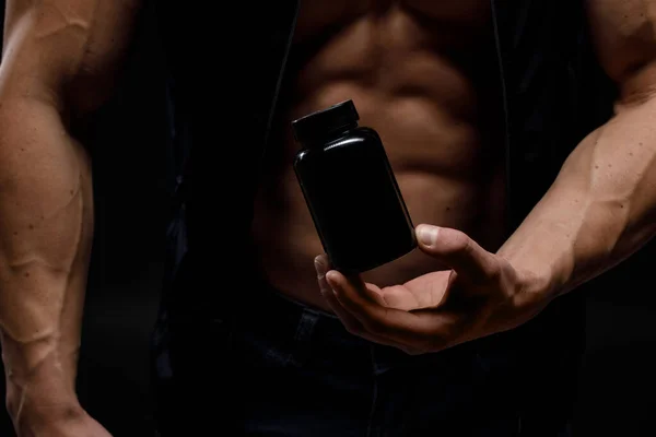 Siyah arka planda protein kavanozu olan kaslı vücut geliştirici. Spor beslenmesi. Vücut geliştirme destek malzemeleri, spor, egzersiz, sağlıklı yaşam tarzı konsepti.
