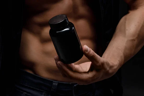 Siyah arka planda protein kavanozu olan kaslı vücut geliştirici. Spor beslenmesi. Vücut geliştirme destek malzemeleri, spor, egzersiz, sağlıklı yaşam tarzı konsepti.