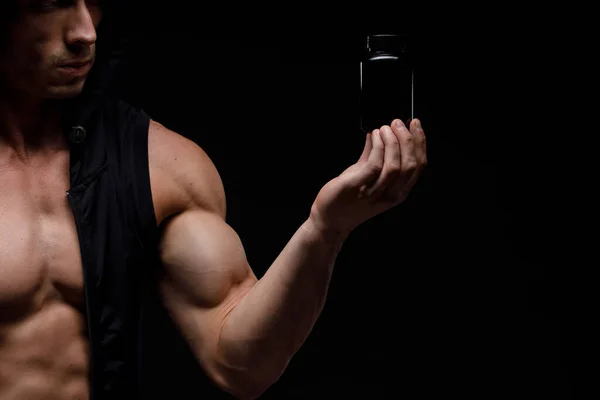 Siyah arka planda protein kavanozu olan kaslı vücut geliştirici. Spor beslenmesi. Vücut geliştirme destek malzemeleri, spor, egzersiz, sağlıklı yaşam tarzı konsepti.