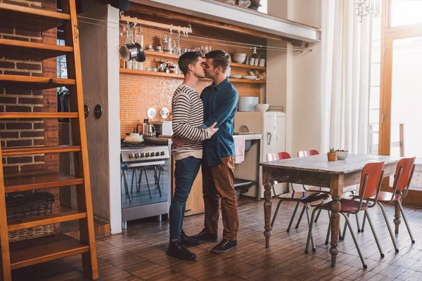 Gay couple standing arm in arm in kitchen — Stock Photo, Image
