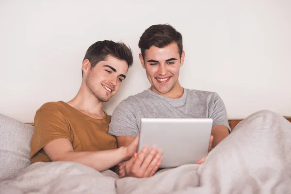 Gay par använda surfplatta liggandes i sängen — Stockfoto