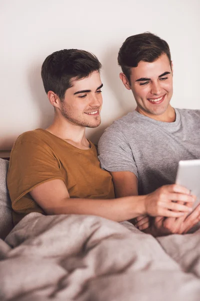 Homosexuální pár pomocí tabletu vleže v posteli — Stock fotografie