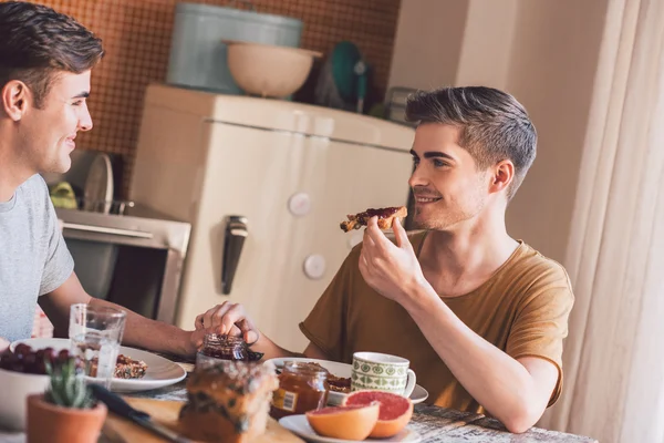 Gay couple talking and eating breakfast — Stock Photo, Image
