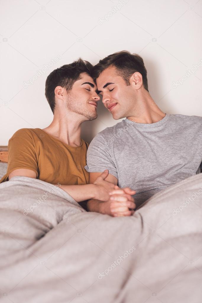 gay couple holding hands together in bed