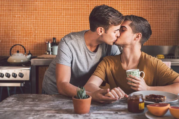 Gay couple kissing together while sitting at kitchen — Stock Photo, Image