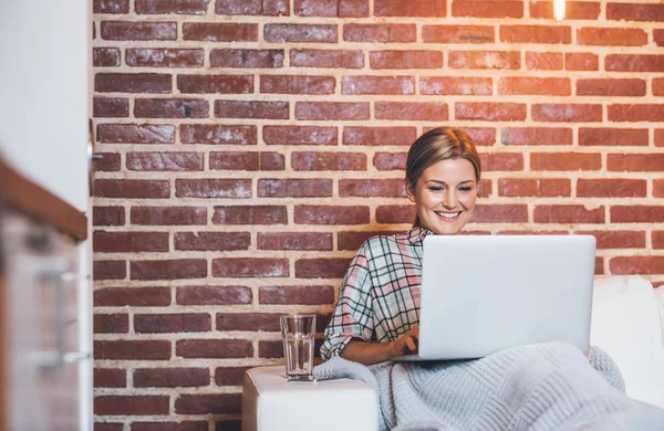 Wanita menggunakan laptop di sofa dibungkus selimut — Stok Foto