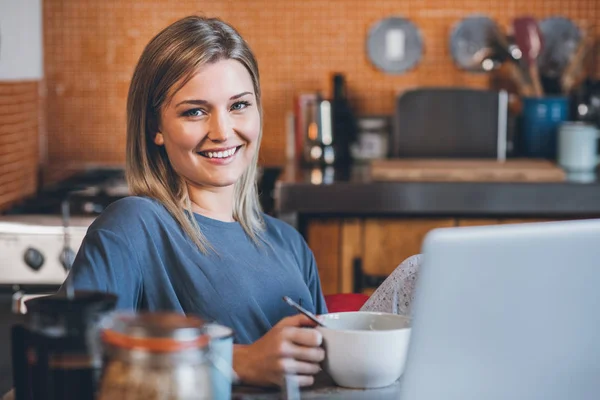 Kahvaltı yemek yerken dizüstü bilgisayar kullanan kadın — Stok fotoğraf