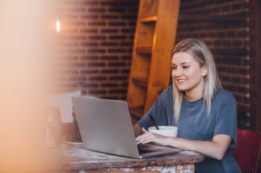 Kahvaltı yemek yerken dizüstü bilgisayar kullanan kadın