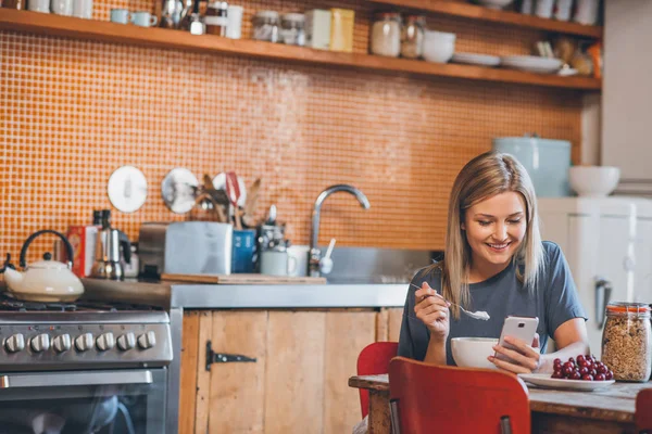 Mujer sentada en la mesa en la cocina usando el teléfono celular — Foto de Stock